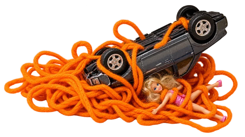 Traffic’s miniature crash: an overturned toy car and doll tangled in orange string